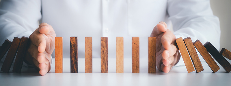 hands stopping wooding blocks in a row from falling - representing risk management