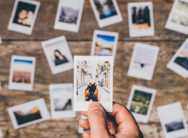 In the foreground, a hand holding a photo of a girl travelling. In the background, many more photos of different  subjects